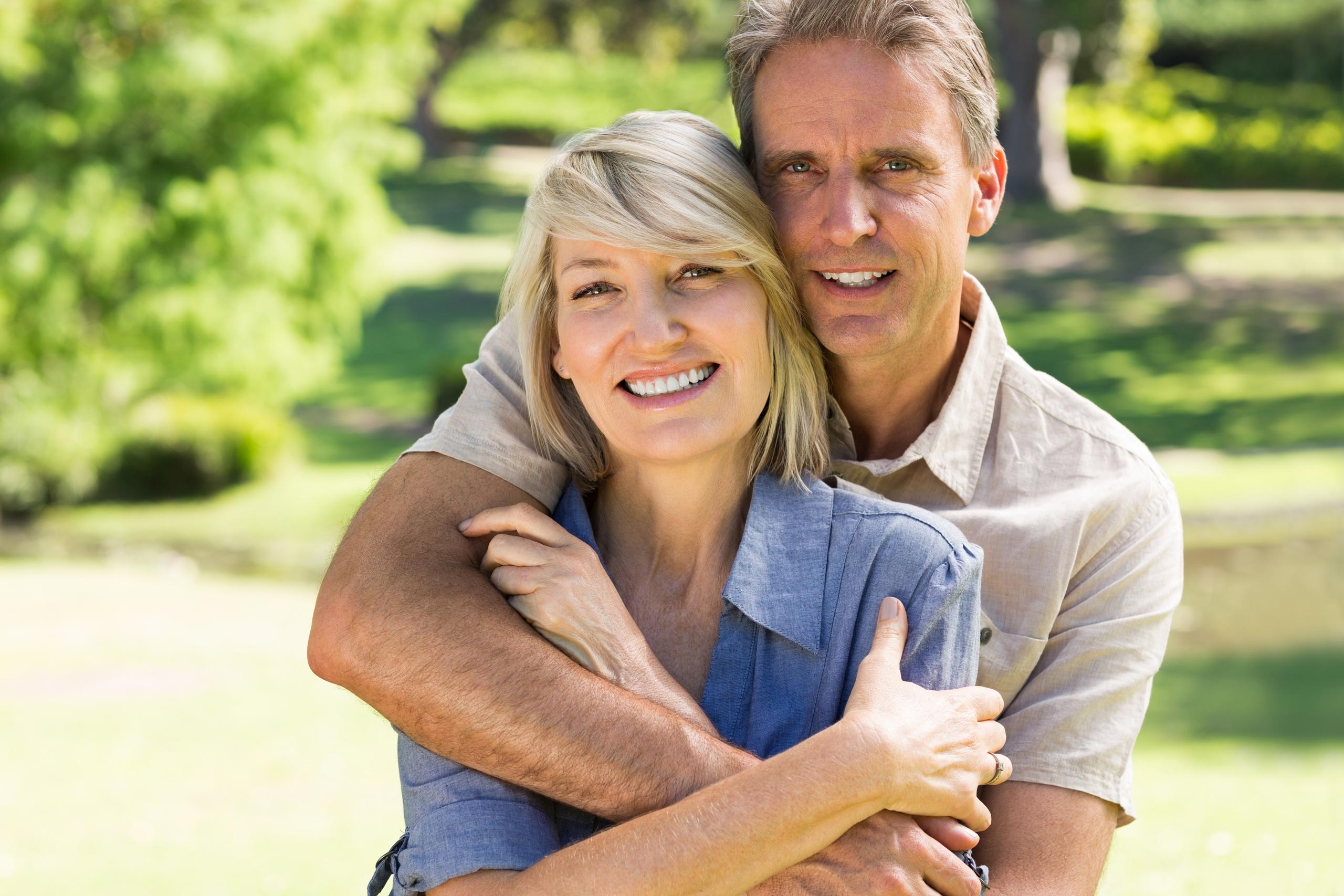 Happy couple, smiling toward the camera outdoors.