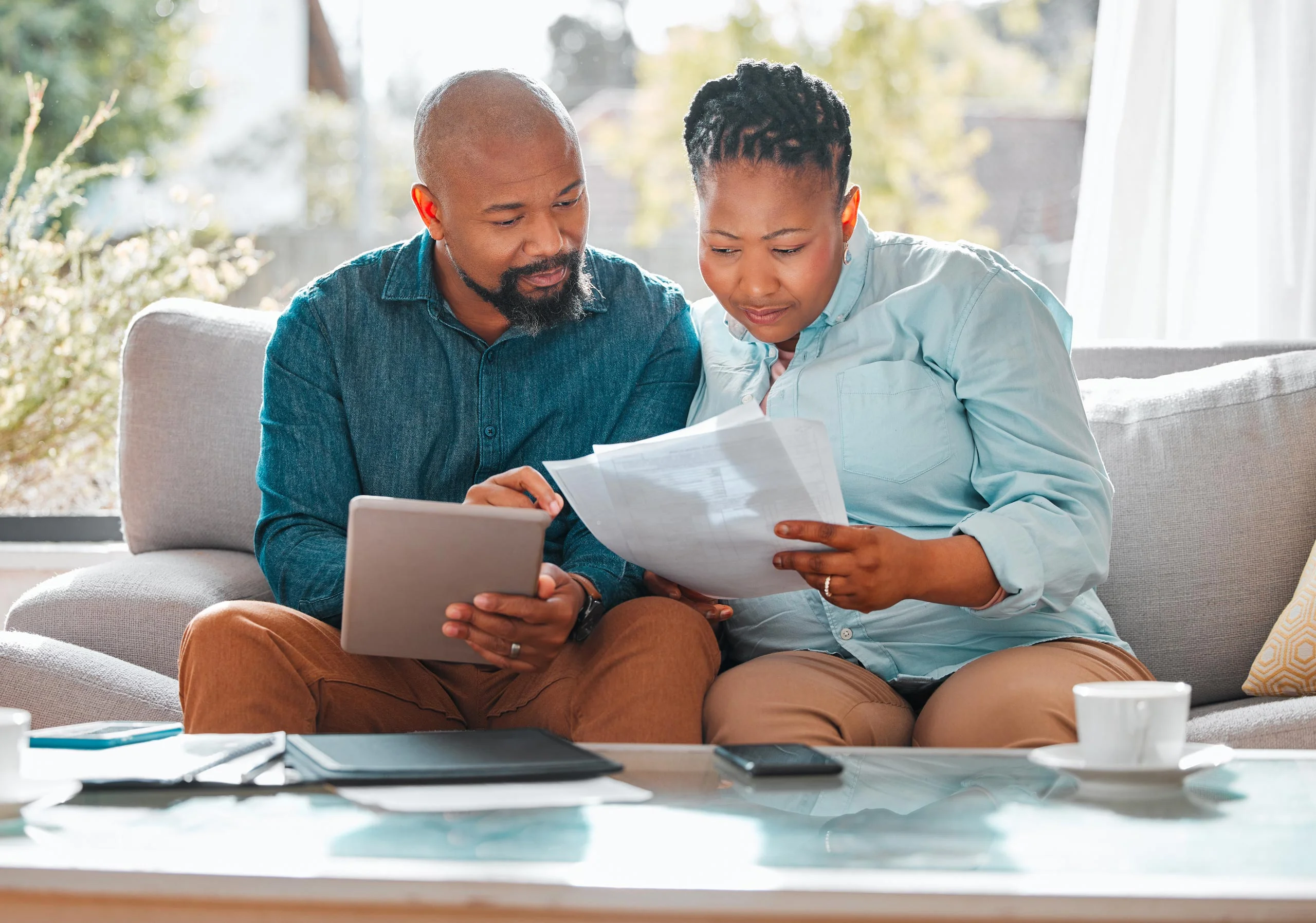 Couple sitting on a light coloured couch, looking at an iPad and information printouts.