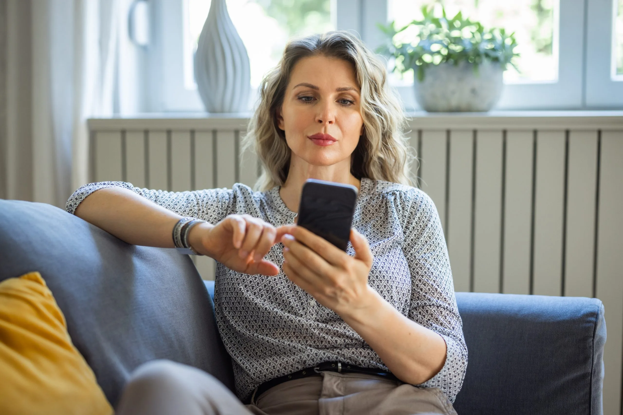 Woman at home, sitting on sofa and using smart phone.